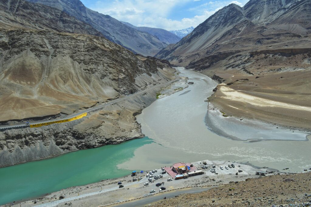 Aerial view of colorful river confluence in mountainous Ladakh landscape under a clear blue sky.
